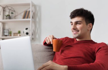 Adam evde kanepede otururken dizüstü bilgisayar ile