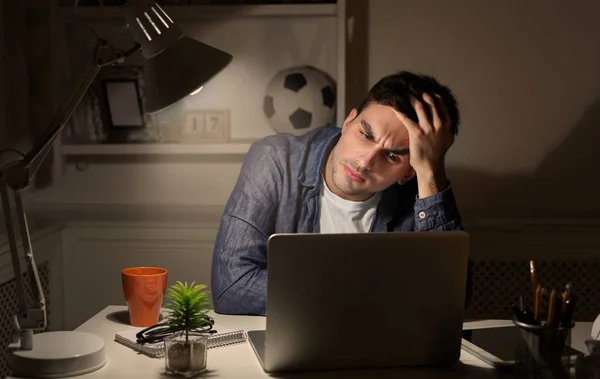 Exhausted man working late at home on laptop