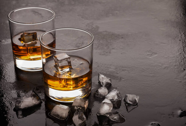 Two glasses of whiskey and ice on black background