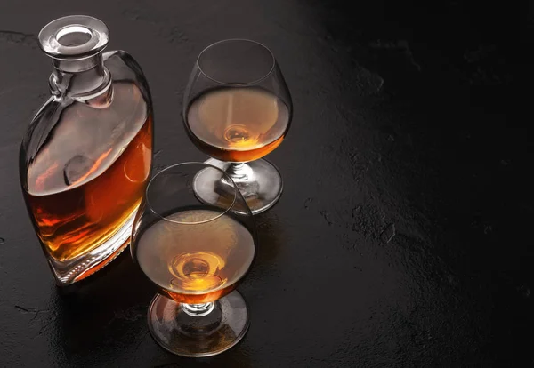 Två glas av brandy eller cognac och flaska på svart — Stockfoto