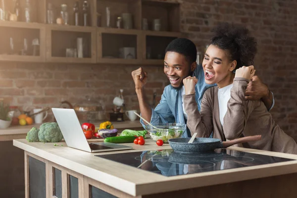 Feliz pareja negra con los brazos levantados cocinando y mirando en el portátil — Foto de Stock