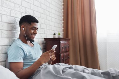 Genç yakışıklı adam yatakta müzik keyfi siyah