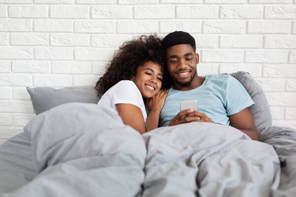 Счастливая пара обнимается в постели со смартфоном
