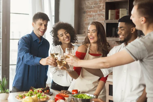 Vrienden rammelende wijnglazen tijdens het koken in de keuken — Stockfoto