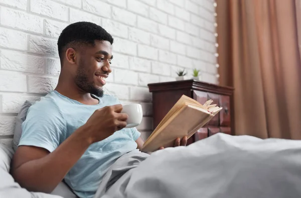 Uomo nero bere caffè e leggere libro a letto — Foto Stock