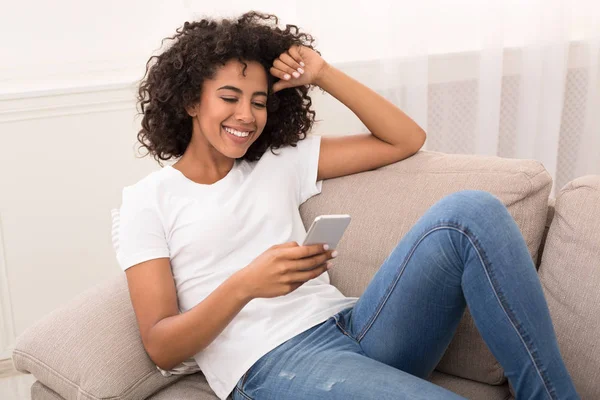 Smiling african-american woman chatting on smartphone at home — Stok Foto