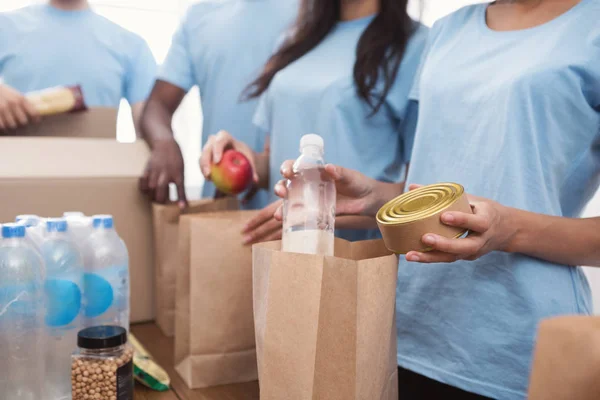 Voluntários embalando alimentos e bebidas em sacos de papel — Fotografia de Stock