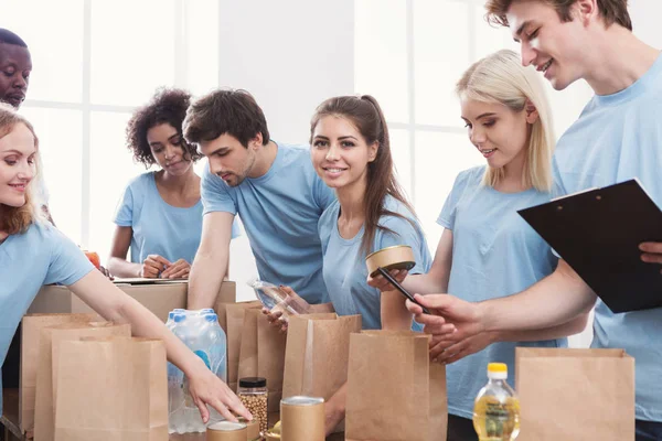 Voluntarios empacando alimentos y bebidas en bolsas de papel — Foto de Stock