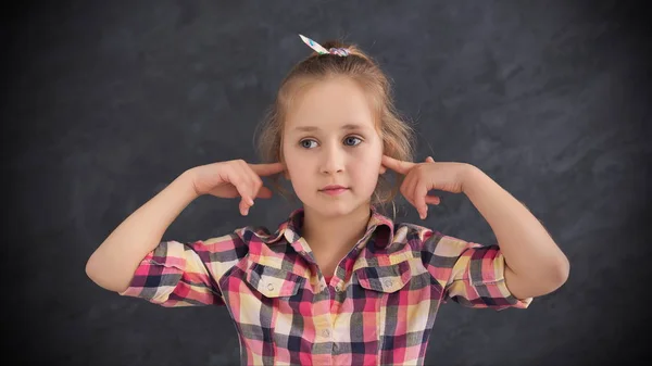 Liten flicka stängt öronen med fingrar på grå bakgrund — Stockfoto