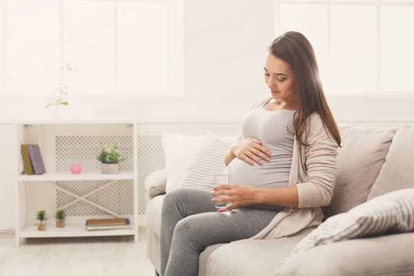 Pregnant woman drinking water sitting on sofa — Stock Photo, Image