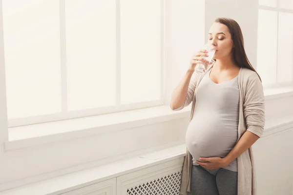 Беременная женщина пьет воду у окна — стоковое фото