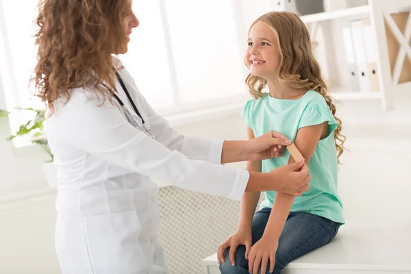 Mädchen lächelt, während Kinderarzt Pflaster klebt — Stockfoto