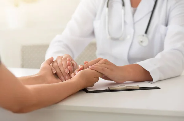 Friendly female doctor holding patient hands sitting at desk — Stock Photo, Image