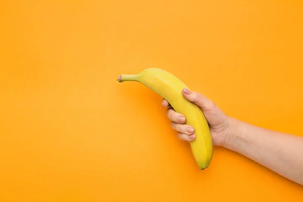 Mano femenina sosteniendo plátano sobre fondo naranja —  Fotos de Stock