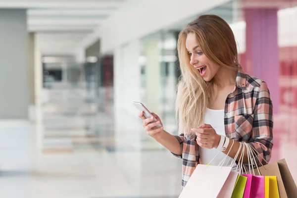 Förvånad kvinna som tittar på telefonen i köpcentrum — Stockfoto