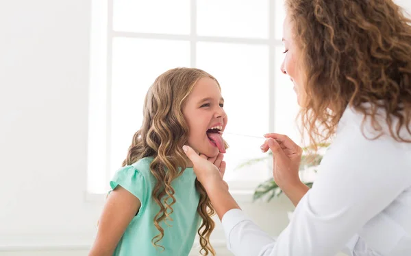 Liten flicka med halsen undersökning med tungspatel — Stockfoto