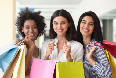 Three excited women with colourful bags shopping in mall clipart