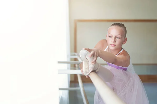 Pequena bailarina se alongando na classe perto do ballet barre — Fotografia de Stock