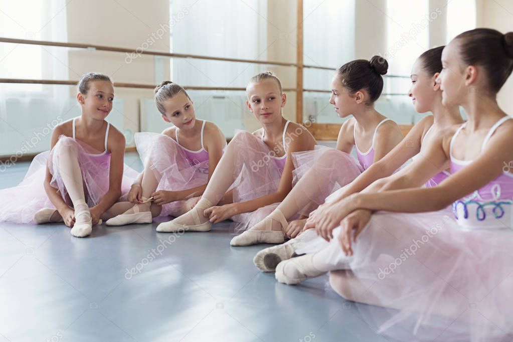 Little ballerinas talking in ballet studio, sitting on floor