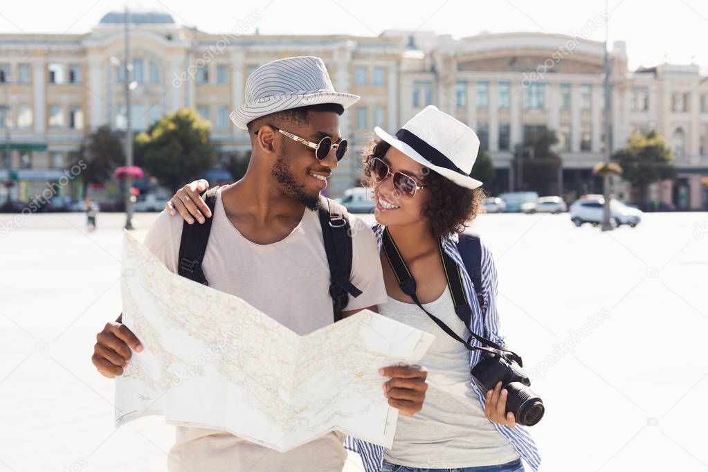 Loving african-american couple traveling and reading map in city