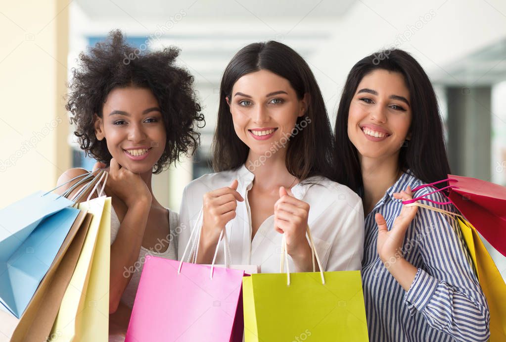 Three excited women with colourful bags shopping in mall