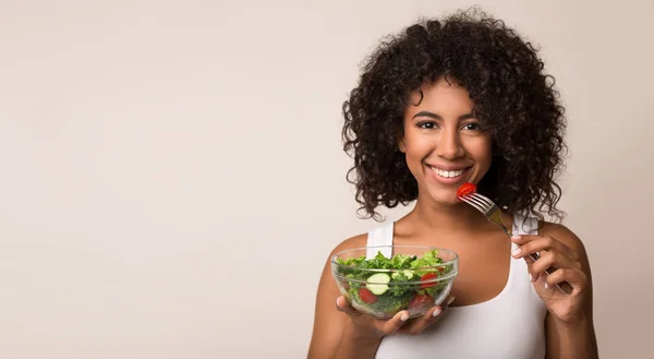 Afroamerikansk kvinna äta grönsakssallad över ljus bakgrund — Stockfoto