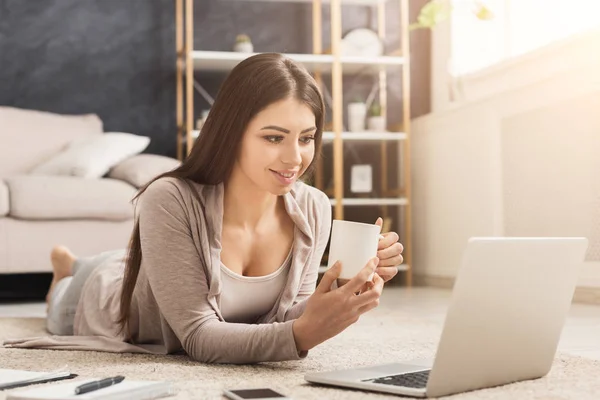 Happy woman chatting on laptop and drinking coffee