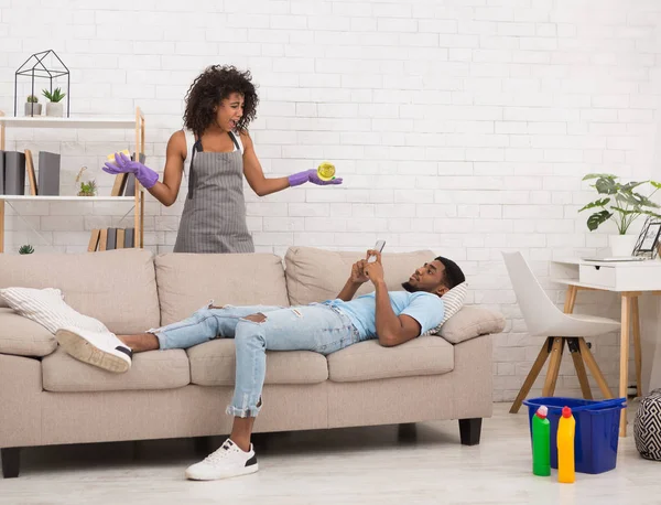 Woman cleaning home while her boyfriend resting on couch — Stock Photo, Image