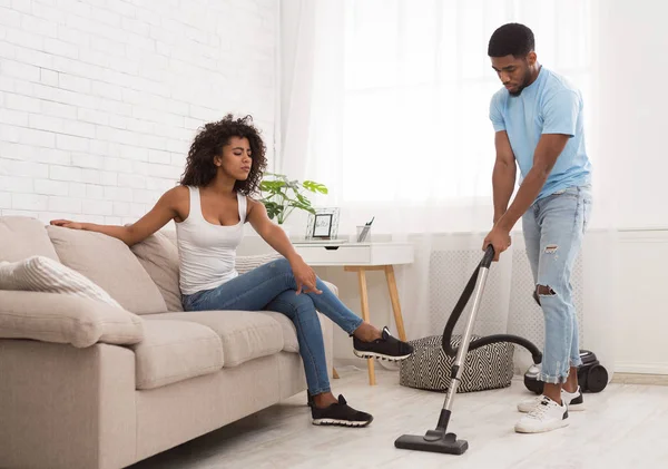 Woman relaxing while black man cleaning apartment — Stock Photo, Image