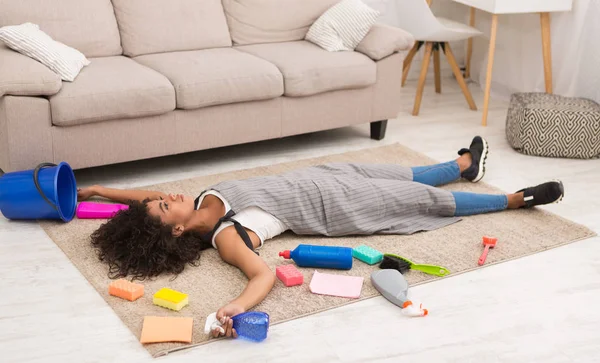 Mulher cansada com suprimentos de limpeza deitada no chão — Fotografia de Stock