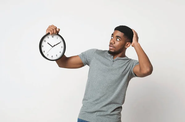 Шокований чорний чоловік тримає настінний годинник над білим тлом — стокове фото
