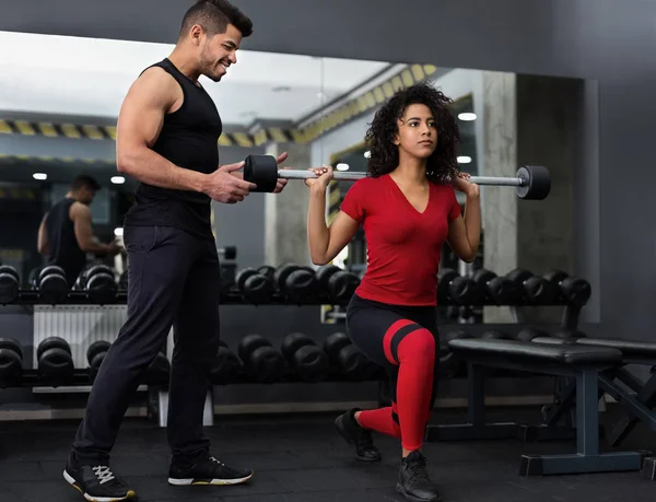 Instrutor pessoal ajudando mulher com agachamentos barbell — Fotografia de Stock