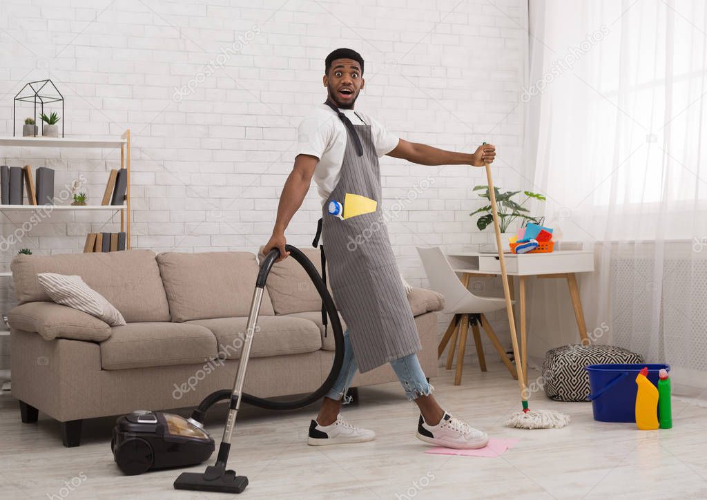 Black man cleaning floor with vacuum cleaner and mop