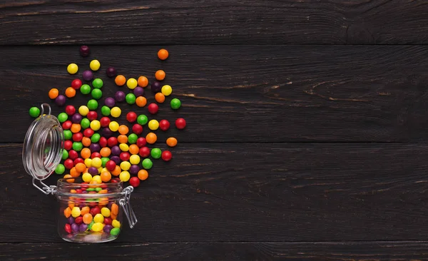 Frasco de vidro com doces coloridos em fundo de madeira — Fotografia de Stock