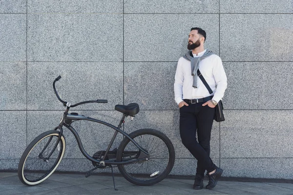 Empresário de pé contra a parede do edifício com sua bicicleta . — Fotografia de Stock