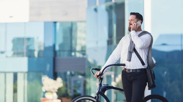 Empresário sorridente falando por telefone celular de pé com bicicleta — Fotografia de Stock