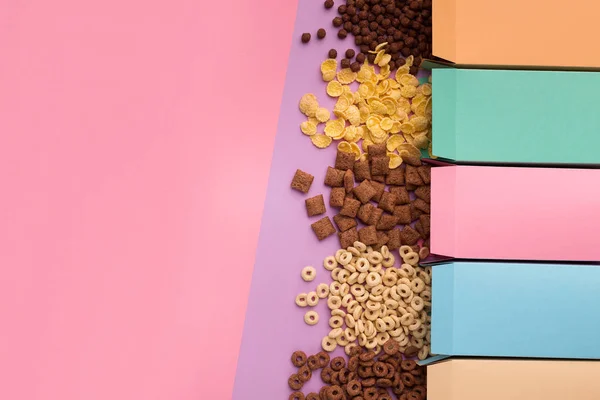 Colorful boxes with scattered cereals on pink background