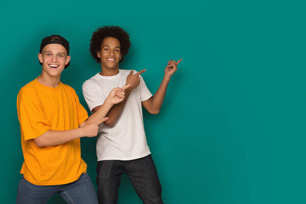 Два счастливых друга указывают пальцем на пространство для копирования на синем фоне
