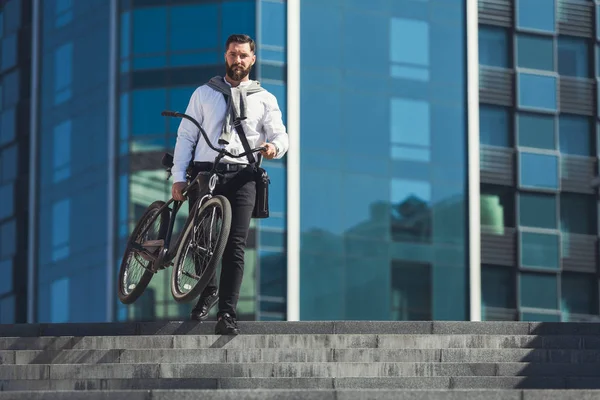 Homem de negócios barbudo carregando sua bicicleta nas escadas — Fotografia de Stock