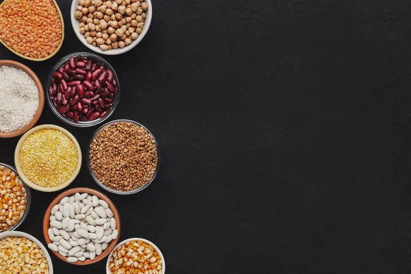 Various grains in different bowls on black background — Stock Photo, Image