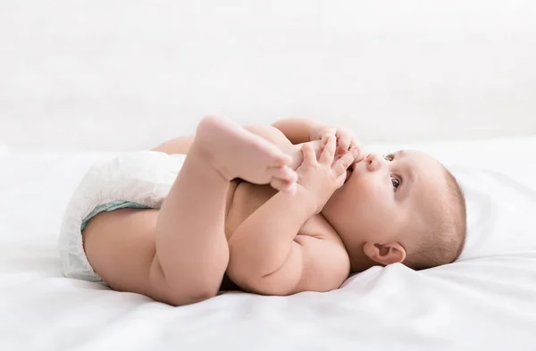 Küçük bebek yatakta yatarken ayak emme — Stok fotoğraf