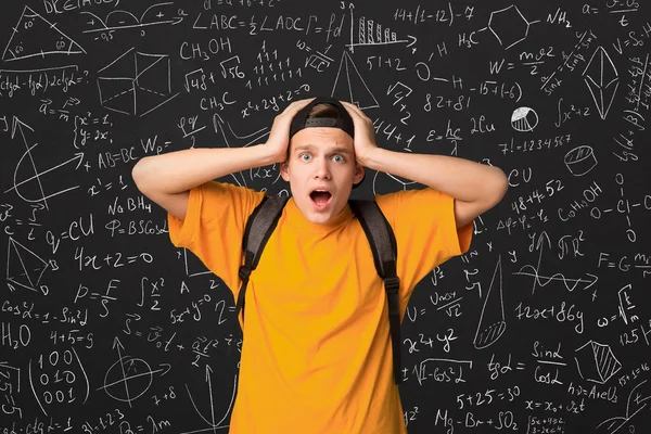 Шокированный студент, стоящий за доской с математическими формулами — стоковое фото