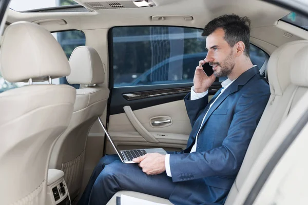 Siempre disponible. Empresario trabajando en el ordenador portátil en el coche — Foto de Stock