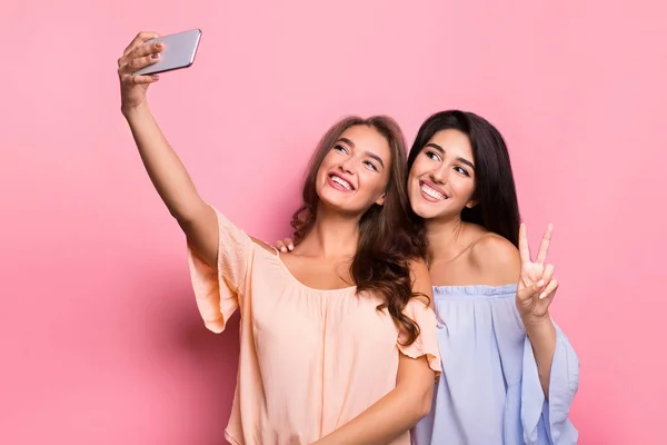 Dos mujeres alegres tomando selfie sobre fondo rosa — Foto de Stock