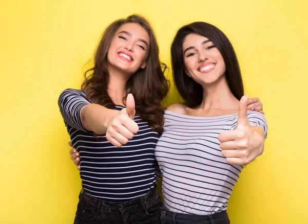 Милі жінки друзі показують великі пальці на жовтому тлі — стокове фото