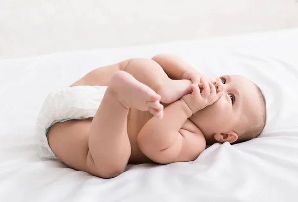 Schattige kleine baby zuigen voet liggend op bed — Stockfoto