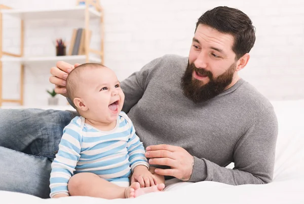 Young bearded man playing with his little baby in bed — Stock Photo, Image