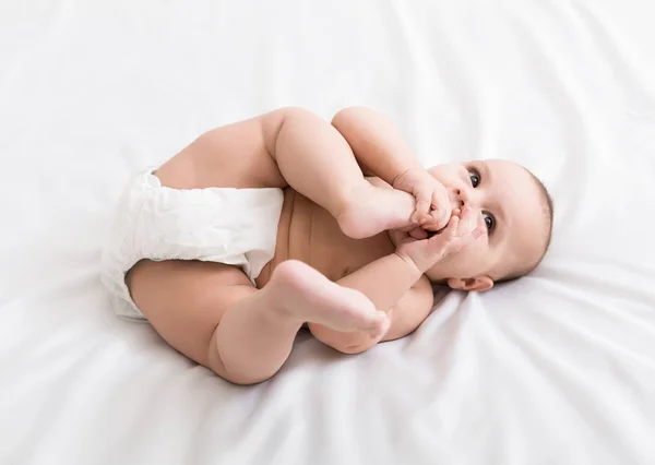 Adorável bebê chupando pé deitado na cama — Fotografia de Stock