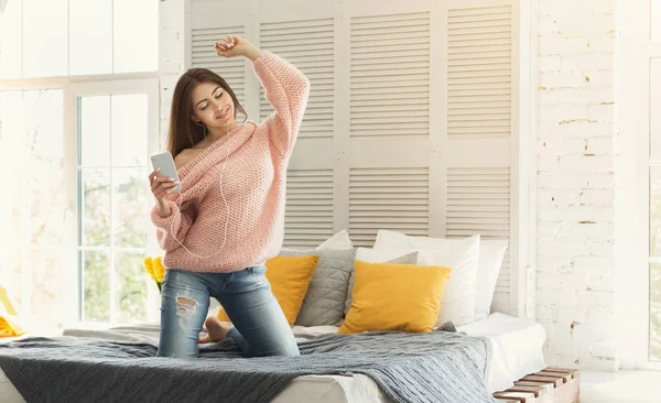 Glad tjej, lyssna på musik på smartphone och dans i sängen — Stockfoto