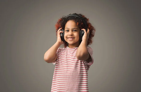 Menina afro em grandes fones de ouvido no fundo estúdio cinza — Fotografia de Stock